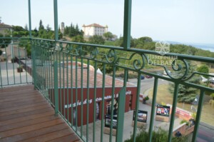 balcon métallique avec platelage bois et garde-corps à barreaux droits incluant des volutes en ferronnerie de coloris vert Provence au village d'Aiguines tout en apercevant le Château d'Aiguines (04) rovence