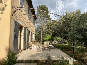 pergola en fer forge fixé contre un mur positionné sur une dalle volutes forgées à la main entouré d'arbres et de végétations Ferronnerie Delbart les Mées Haute Provence 04.