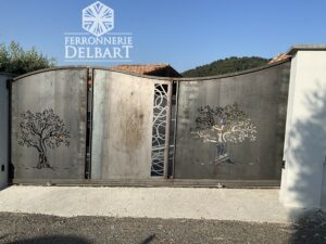 portail asymétrique en acier coulissant à motifs découpe laser fixé entre des piliers béton blanc sous un ciel bleu. Ferronnerie Delbart les Mées Haute-Provence 04.