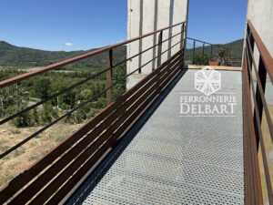 rampe en acier marche caillebottis fixé entre deux poteaux ciment entouré de végétations sous un ciel bleu. Ferronnerie Delbart les Mées en Haute-Provence.