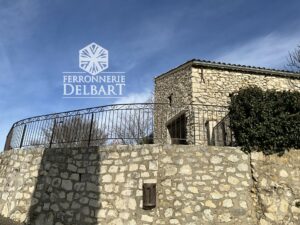 garde-corps en fer forgé barreaux droits volutes à la forge garde-corps fixé sur muret en pierres sous un ciel partiellement nuageux ferronnerie Delbart Haute-Provence 04.